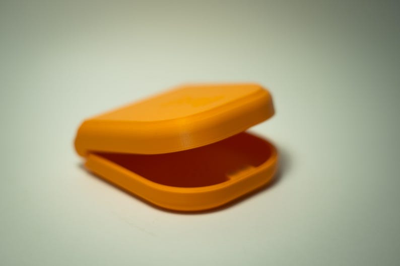 Puede incluir: Un recipiente naranja abierto y con bisagras. El contenedor es rectangular con esquinas redondeadas y una tapa curva. El interior es visible y el contenedor parece estar hecho de pl&aacute;stico.
