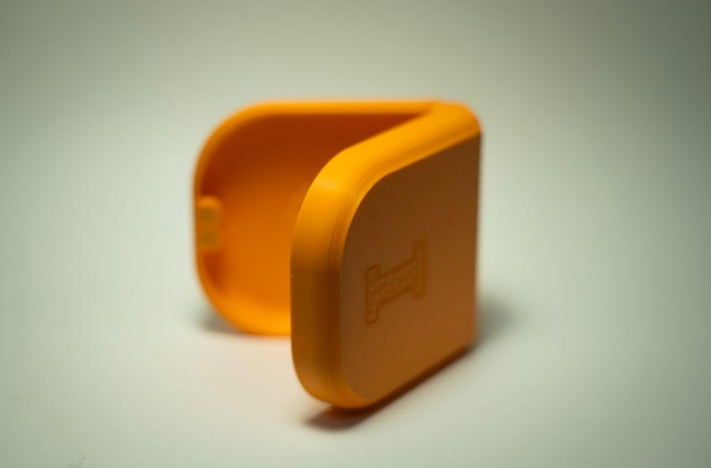 Puede incluir: Carcasa naranja brillante, con bisagras y forma rectangular redondeada. La carcasa est&aacute; abierta, revelando el interior. Un peque&ntilde;o dise&ntilde;o en relieve es visible en la parte delantera. La carcasa est&aacute; hecha de un material liso y s&oacute;lido.