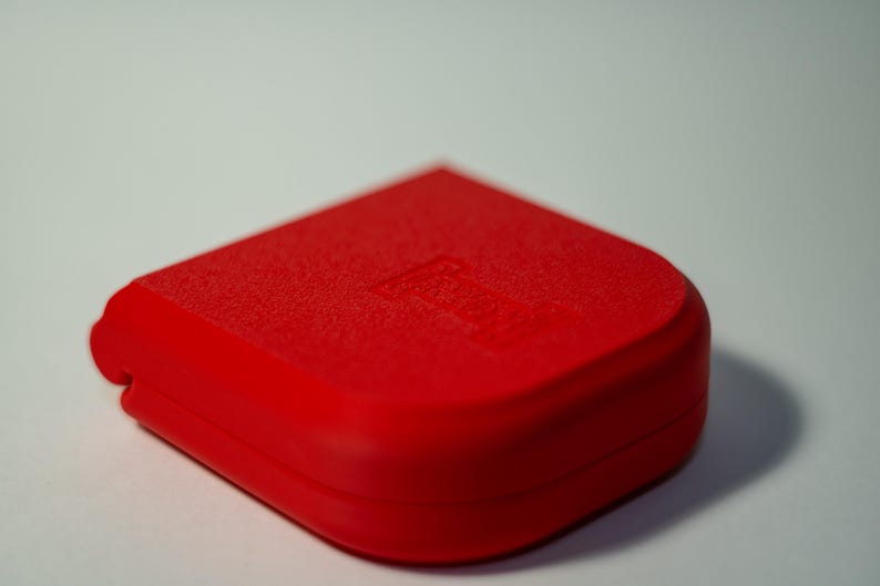 Puede incluir: Un objeto rojo brillante, de forma cuadrada con esquinas redondeadas. La superficie superior tiene una apariencia texturizada, y un dise&ntilde;o sutil es visible. El objeto se encuentra sobre un fondo blanco liso, resaltando su color vibrante y forma.