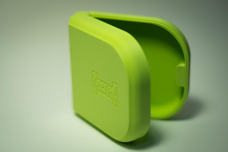 Puede incluir: Un estuche rectangular verde lima con bordes redondeados, parcialmente abierto para revelar un interior verde m&aacute;s claro. El exterior presenta un s&iacute;mbolo de cama en relieve. El estuche est&aacute; hecho de un material mate y liso.