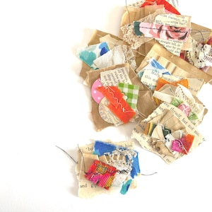May include: A selection of handmade fabric and paper art pieces. The pieces incorporate torn paper, lace, and colourful fabric scraps stitched together. Colours include orange, pink, blue, green, and floral patterns. The art pieces are arranged on a white background.