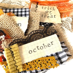 May include: A layered fabric collage featuring hessian, black and white gingham, orange lace, and black lace. The collage includes paper scraps with the printed text "trick or treat" and "october" alongside a mustard yellow textured fabric strip.