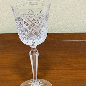 May include: A clear crystal wine glass with a diamond pattern and a long stem. The base of the glass has a starburst design.