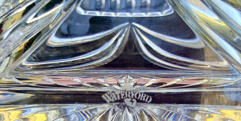 May include: Close-up of a clear crystal object with a geometric design. The word "WATERFORD" is etched into the crystal. The crystal has a reflective quality, with light refracting through the patterned surface.