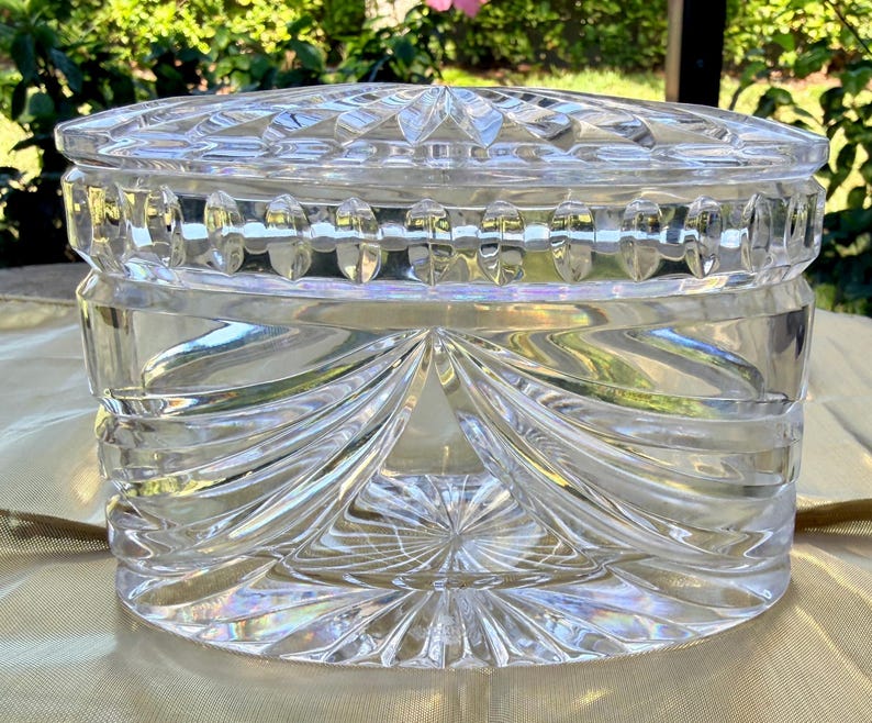 May include: A clear, cut-glass jar with a lid. The jar has a round shape with a decorative pattern of vertical and horizontal cuts. The lid has a starburst design. The jar is likely used for storage or display.