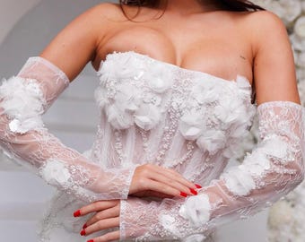 May include: White strapless wedding dress with a lace bodice and floral embellishments. The dress features long, sheer lace gloves with floral accents.