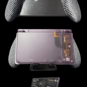 May include: A handheld gaming console with a translucent purple shell and textured gray side grips. The device features an internal gold-colored component visible through the casing, a black stand labeled OMOTON, and a screen displaying a menu interface.