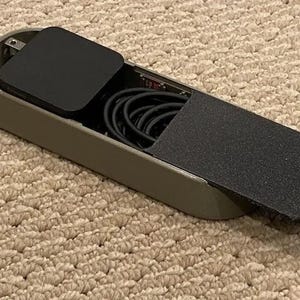 May include: A gray travel case with a black lid and a black power adapter inside. The case has a black fabric lining and a black cord coiled inside.