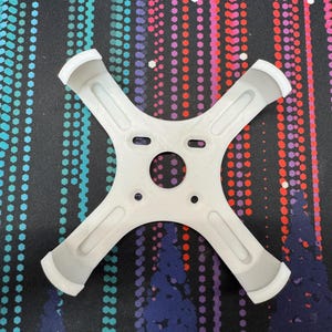 May include: A white plastic 3D printed drone propeller guard with four arms and a central hub.