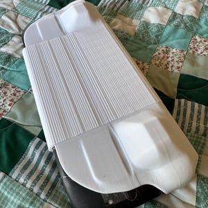 Puede incluir: Estuche de plástico blanco con textura acanalada y base negra. El estuche tiene una forma redondeada y una superficie lisa.