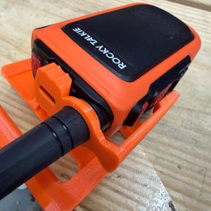 May include: An orange and black Rocky Talkie radio with a black antenna, mounted on an orange holder. The radio has the words "ROCKY TALKIE" printed on the top. The holder is designed to secure the radio.