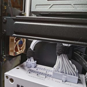 May include: Internal view of a computer case. A beige fan is visible, mounted on a black frame. White cables are neatly bundled and connected to a white power supply unit. The image shows the internal wiring.