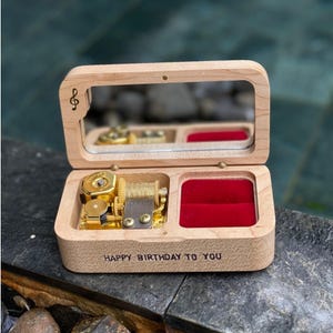 May include: A wooden music box with a mirrored lid and a gold-colored musical mechanism. The box has a red velvet compartment and the words "HAPPY BIRTHDAY TO YOU" are engraved on the front.