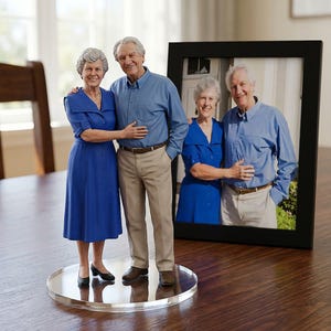 May include: A 3D-printed figurine of an elderly couple, standing on a clear circular base. The woman wears a blue dress, and the man wears a blue shirt and khaki pants. A framed photo of the couple is in the background.