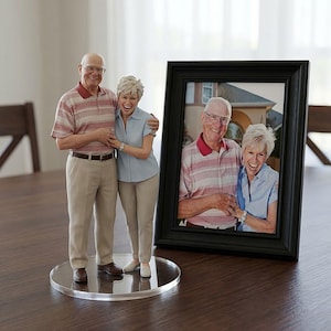 May include: A 3D-printed figurine of an elderly couple, standing on a clear acrylic base, next to a framed photograph of the same couple. The figurine and photo depict the couple smiling and embracing. The man wears a striped polo shirt and khaki pants.