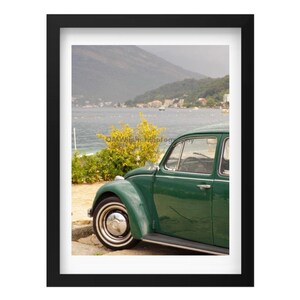 May include: A vintage green Volkswagen Beetle parked on a beach with a view of a bay and mountains in the distance.