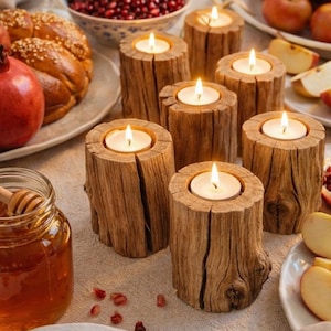 Può includere: Una tavola festosa con candele accese in portacandele di legno, circondata da mele, melograni, pane challah e miele. L'illuminazione calda e gli elementi naturali creano un'atmosfera accogliente.