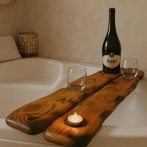 Puede incluir: Una bandeja de baño de madera oscura, con una botella de vino Asti, dos copas y una vela encendida. La bandeja abarca el ancho de una bañera blanca, creando un ambiente relajante de spa.