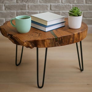Puede incluir: Una mesa auxiliar redonda de madera con patas de horquilla negras. La tapa es una sección transversal de un tronco de árbol. Una taza verde claro, dos libros y una pequeña planta suculenta en maceta están encima. La mesa tiene unos 76 cm de diámetro.