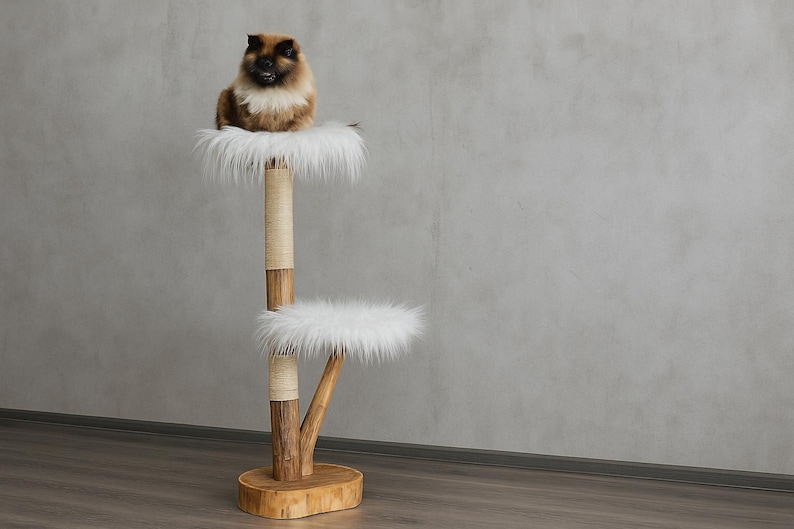 May include: A multi-level cat tree with a brown and white cat perched on the top level. The cat tree has two platforms covered in white faux fur. The structure is made of wood and rope, with a round base.