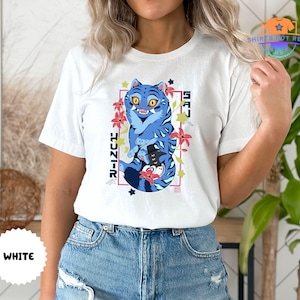 May include: White t-shirt featuring a blue tiger graphic with the text "SAJ HUNIR" in a rectangular frame. The tiger design includes floral accents and stars. The shirt is made of a soft material.