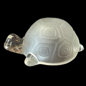 Pode incluir: Uma figura de tartaruga de vidro fosco com um design de casca detalhado. A tartaruga é branca e tem um acabamento liso e polido.