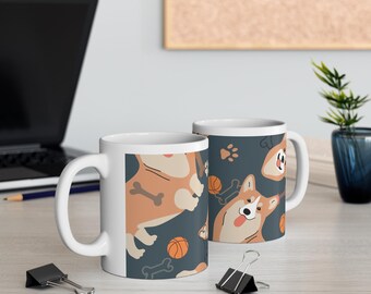 Könnte beinhalten: Zwei weiße Keramikbecher mit einem verspielten Corgi-Hunde-Design. Die Becher haben einen dunkelblauen Hintergrund mit Illustrationen von Corgis, Basketbällen, Pfotenabdrücken und Knochen. Die Becher stehen auf einer hellen Oberfläche.