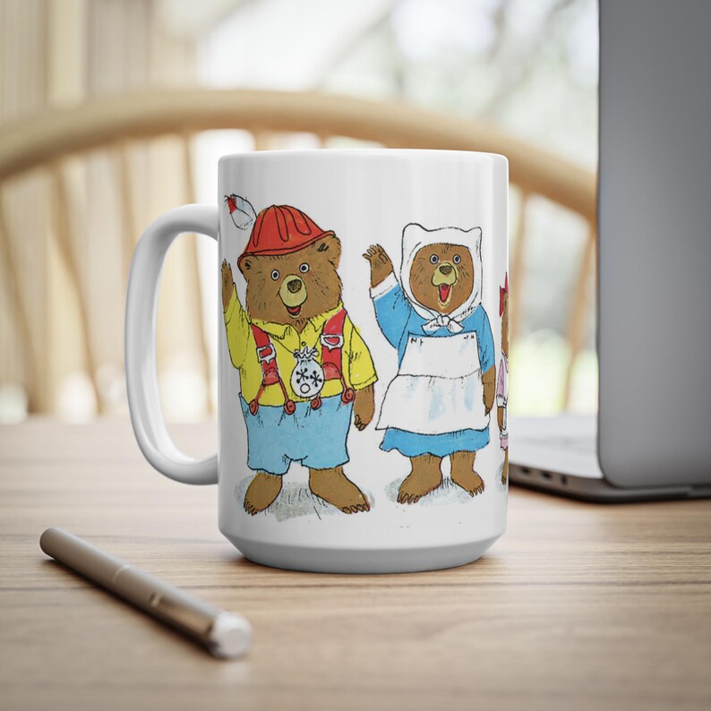May include: White ceramic mug with a colorful illustration of three bears wearing different costumes. The bears are wearing a red and white hat, a white dress with a blue apron, and a pink dress. The mug has a handle on the left side.