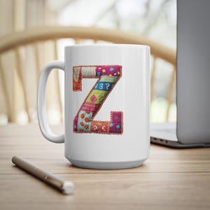 Puede incluir: Taza de cerámica blanca con una letra Z de patchwork en colores rosa, verde, naranja y azul. La letra está rodeada por un hilo dorado.
