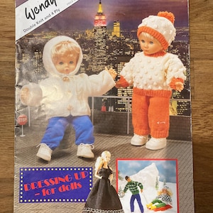 Könnte beinhalten: Ein Wendy Strickmusterheft mit dem Titel Dressing Up - for dolls, das zwei Puppen in gestrickten Pullovern, Mützen und Hosen vor der Skyline von New York zeigt. Das Cover enthält ein kleines Bild von Puppen in Winterkleidung und einem schwarzen Kleid.