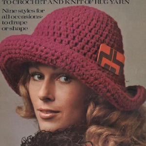 May include: A burgundy crochet hat with a wide brim and a decorative square accent. The hat is made of thick yarn and has a textured appearance. The image also includes text that reads "TO CROCHET AND KNIT OF RUG YARN" and "Nine styles for all occasions - to drape or shape."