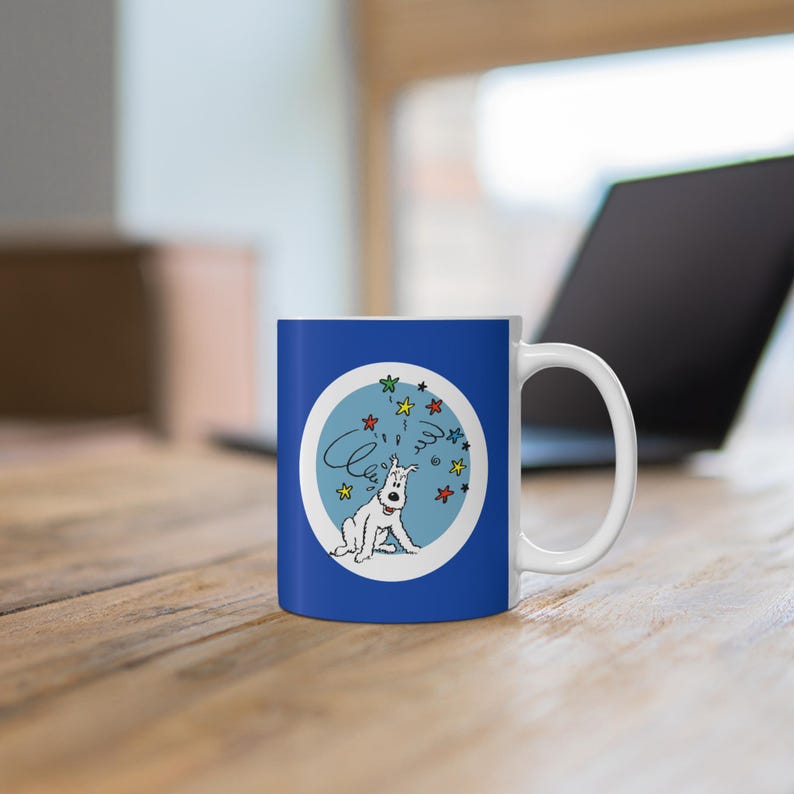 May include: A blue and white ceramic mug featuring a cartoon dog with a thought bubble and stars. The dog is white with black details, sitting inside a light blue circle. The mug has a white handle and is on a wooden surface.