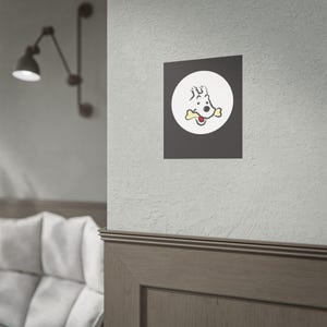Puede incluir: Una impresi&oacute;n enmarcada con un perro de dibujos animados con un hueso en la boca, sobre un c&iacute;rculo blanco sobre un fondo gris oscuro. El perro est&aacute; representado en negro y rojo. La impresi&oacute;n est&aacute; montada en una pared.