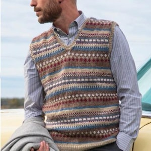 May include: A knitted vest with a V-neck, featuring a pattern in brown, blue, and red. The vest is worn over a striped shirt. The person is wearing a grey flat cap and dark trousers. The overall style suggests a classic, casual look.
