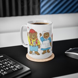 May include: White ceramic coffee mug with a colorful illustration of three bears wearing clothes. The bears are a firefighter, a nurse, and a chef. The mug is sitting on a cork coaster.