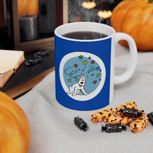 May include: A white ceramic mug with a blue exterior featuring a cartoon dog design. The dog is white with a blue background and colorful stars. The mug has a white handle and is filled with a dark liquid.