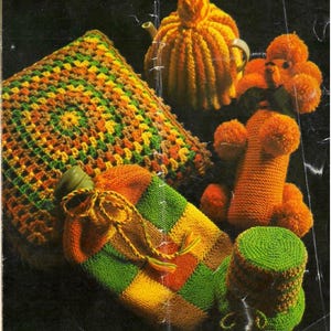 May include: A collection of handmade knitted items in shades of orange, green, and yellow. Includes a teapot cozy, hot water bottle cover, pillow, and a small hat. The items are arranged on a dark background.