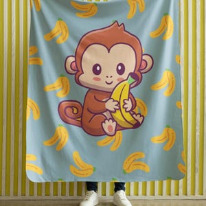 May include: A light blue blanket with a cartoon monkey holding a banana. The monkey is brown with a light pink face and ears. Yellow bananas are scattered across the blanket's surface.
