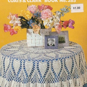 May include: A crocheted tablecloth with a scalloped edge, covering a round table. A woven basket with colorful flowers sits on the table, along with two framed photos. The text "ALL TIME FAVORITES" is at the top.