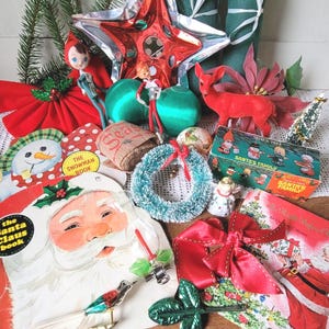 Pode incluir: Uma coleção de decorações de Natal vintage, incluindo um livro do Pai Natal, um livro de boneco de neve, uma estrela vermelha, duas figuras de elfos, um veado vermelho, uma pequena coroa, uma caixa Santa's Family, um pássaro e laços vermelhos.