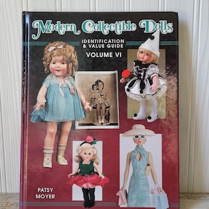 May include: A hardcover book titled "Modern Collectible Dolls" with the subtitle "Identification & Value Guide Volume VI." The cover features images of vintage dolls in various outfits. The author's name, Patsy Moyer, is printed at the bottom.