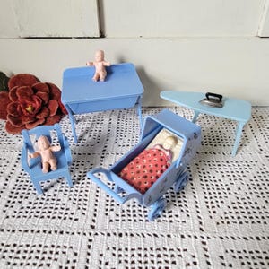 May include: A set of miniature light blue plastic furniture including a baby carriage with a red patterned blanket, a high chair, a table, and an ironing board with a small iron. Two small plastic baby figurines are included in the set.