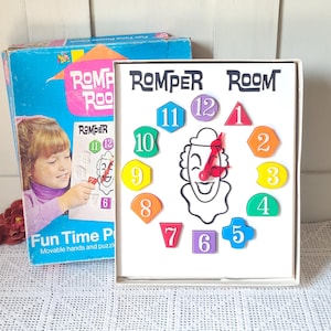 Könnte beinhalten: Ein Romper Room Fun Time Puzzle-Uhr-Spiel mit einer weißen Tafel, die in der Mitte eine schwarze Strichzeichnung eines Clown-Gesichts zeigt. Zwölf bunte geometrische Formen mit den Zahlen eins bis zwölf sind kreisförmig um das Gesicht angeordnet.