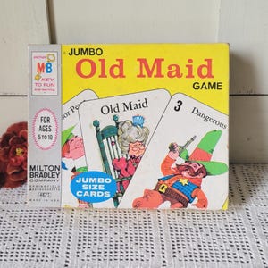 May include: A yellow Milton Bradley Jumbo Old Maid card game box featuring illustrations of a character in a rocking chair and a cowboy. The box includes text such as JUMBO Old Maid GAME, FOR AGES 5 TO 10, and JUMBO SIZE CARDS on the front cover.