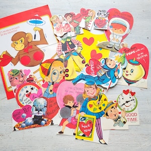 May include: A collection of vintage Valentine's Day cards with various illustrations. The cards feature images of a monkey, cowboy, astronaut, and other characters. Some cards are heart-shaped and include text like "Be My Valentine" and "Love You!"