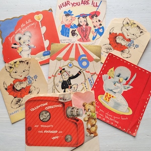 May include: A collection of seven vintage-style greeting cards featuring colorful illustrations of animals and characters. Designs include a bear with a camera, a monkey in a circus tent, a kitten in a red skirt, and a bird with a heart-shaped cake.