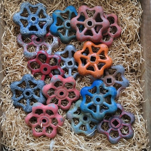 Könnte beinhalten: Eine Sammlung von Vintage-Ventilgriffen in Blumenform in verschiedenen Farben, darunter Blau, Rot und Orange. Die Griffe sind in einer Holzkiste mit Stroh angeordnet.