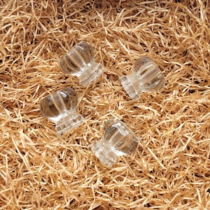 May include: Four clear glass cabinet knobs with a faceted, mushroom-shaped design. Each knob features a rounded top with vertical ridges and a flat, circular base, providing a transparent and reflective appearance for furniture hardware.