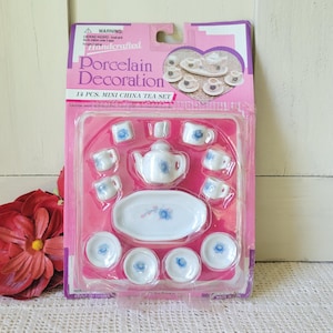 May include: A 14-piece miniature porcelain tea set in a pink package. The set includes a teapot, cups, saucers, and a serving tray, all decorated with blue floral designs. The package reads "Porcelain Decoration".