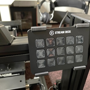 May include: Black Stream Deck with 15 illuminated buttons, mounted on a black frame. The Stream Deck logo is visible. The device is part of a gaming or streaming setup.
